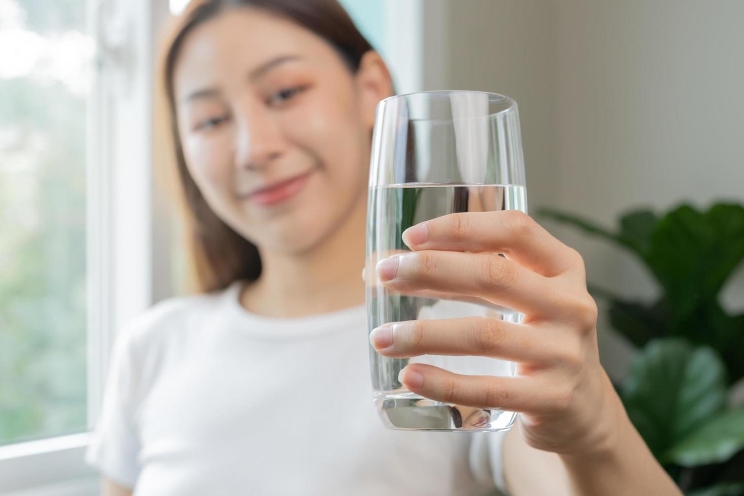 Happy beautiful, asian young woman, girl drinking, sip fresh glass of water for hydration of body, holding transparent glass in her hand, thirsty at home. Health care, healthy lifestyle concept. photo