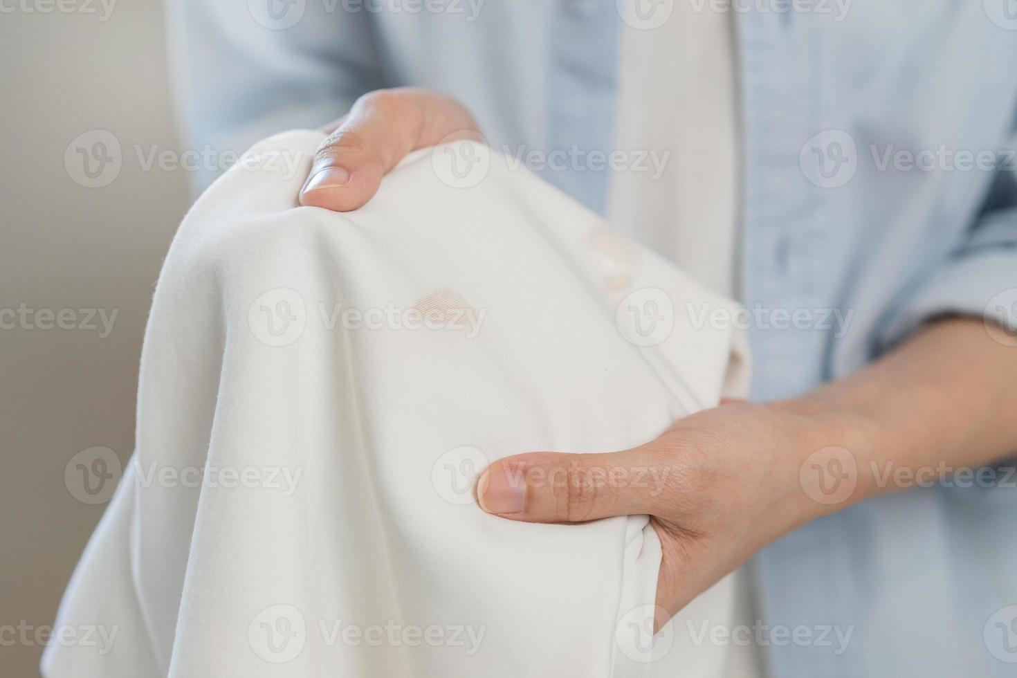 Housewife, asian young woman hand in holding shirt, showing making stain, spot dirty or smudge on clothes, dirt stains for cleaning before washing, making household working at home. Laundry and maid. photo