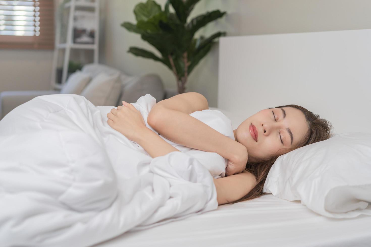 Sweet dreams, attractive smile pretty asian young woman, girl sleeping in comfortable bed lying on soft pillow resting, keeping eyes closed while with covered blanket in cozy white bed in the morning. photo