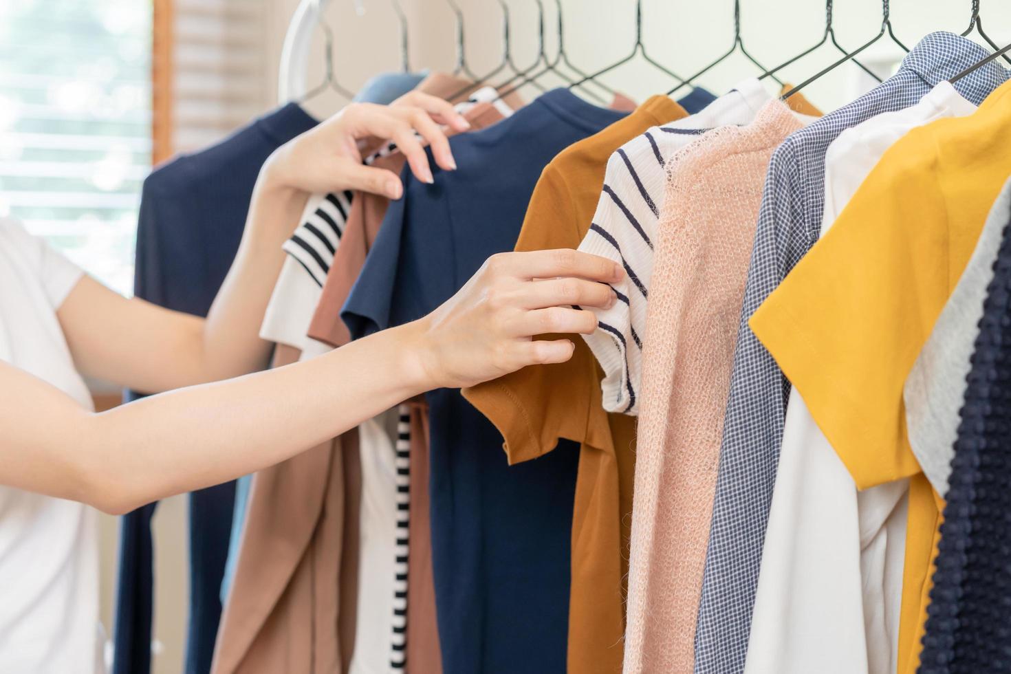 Choice of clothes, Nothing to wear asian young woman, girl hand in choosing dress, outfit on hanger in wardrobe in room closet at home. Deciding what to put on which one. photo