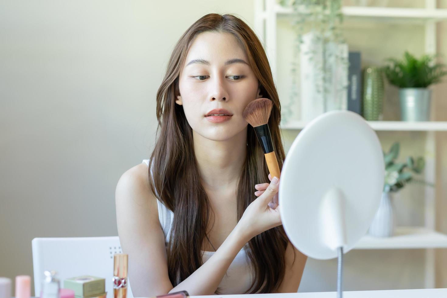 contento belleza blogger concepto, linda asiático joven mujer, niña sonrisa, hacer arriba cara por aplicando cepillo sonrojo polvo en su mejilla, mirando a el espejo. personas Mira con natural Moda estilo, Copiar espacio. foto