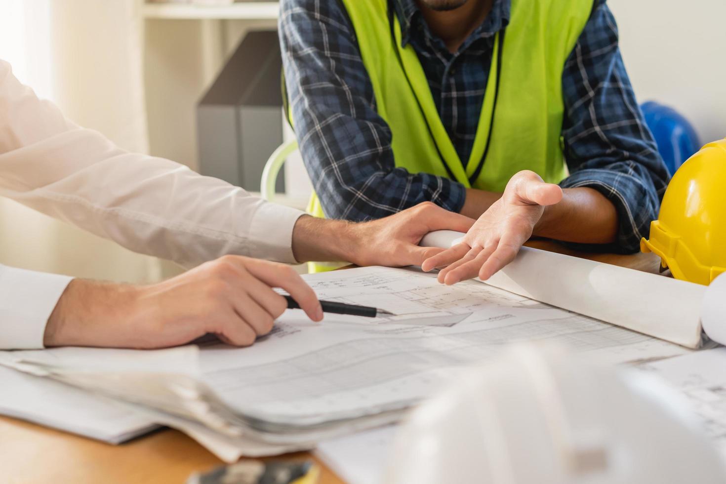 Builder team, hand of asian, caucasian young engineer, architect two man are discussing construction drawing on blueprint follow project to build an industrial plan at site. Engineering worker people. photo