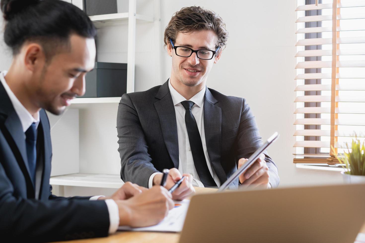 Business meeting, two caucasian, asian group man use tablet brainstorm analyzing on graph data of cost plan or document, paperwork and discussing in board room on table. People working conference room photo