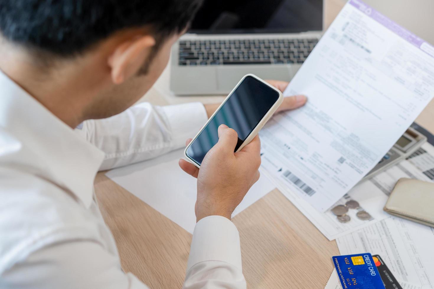 costo, presupuesto asiático joven hombre calcular gastos, gasto y cheque desde factura, utilizar teléfono inteligente, móvil teléfono pagar pago Internet en línea de crédito tarjeta a hogar. tecnología de finanzas, financiero. foto