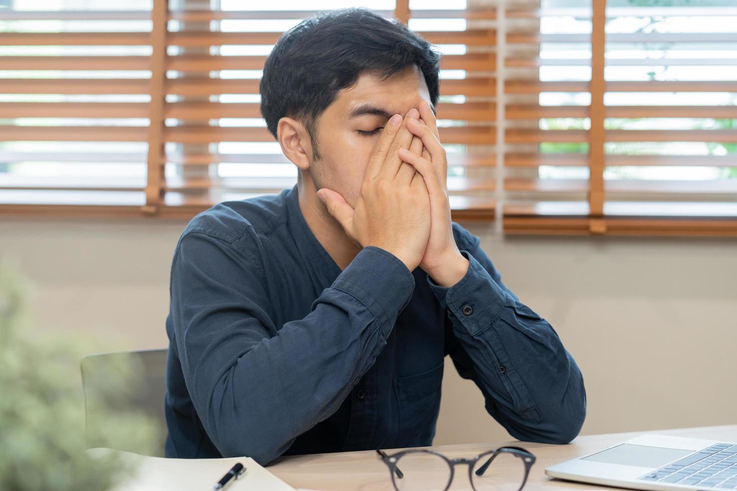 empresario exhausto, mano de estrés asiático joven negocio hombre trabajando en dolor de cabeza, sufrir en difícil trabajo mientras utilizar ordenador portátil computadora a oficina. tiempo extraordinario trabajo, deuda problema y desesperación gente. enfermo indispuesto foto