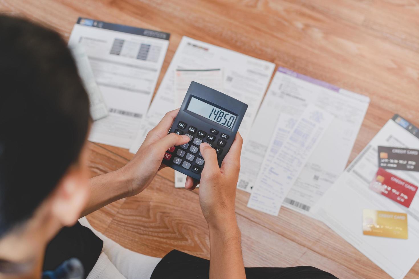 Top view financial owe asian young man sitting suffer, stressed and confused by calculate expense from invoice, credit card bill no money to pay mortgage or loan. Debt, bankrupt or bankrupt people. photo