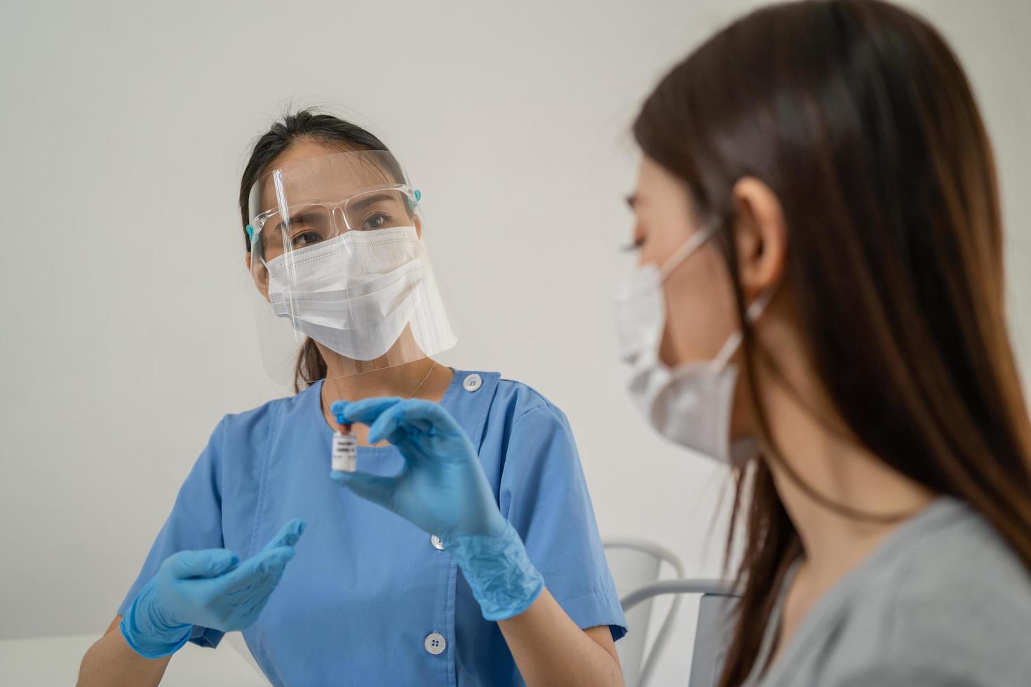 covid-19,coronavirus asiático joven médico o enfermero mujer participación frasco vacuna, hembra paciente preparar inyectar a brazo. vacunación, inmunización o enfermedad prevención en contra gripe o virus pandemia concepto. foto