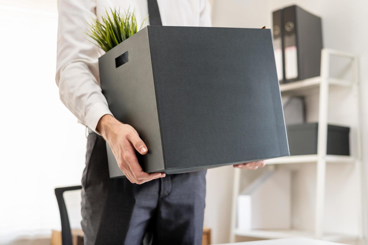 Unemployed, quite job. Desperate caucasian young businessman resigning from company, hand in holding cardboard, packing belongings into box, layoff or changing work. Resignation, employment concept. photo