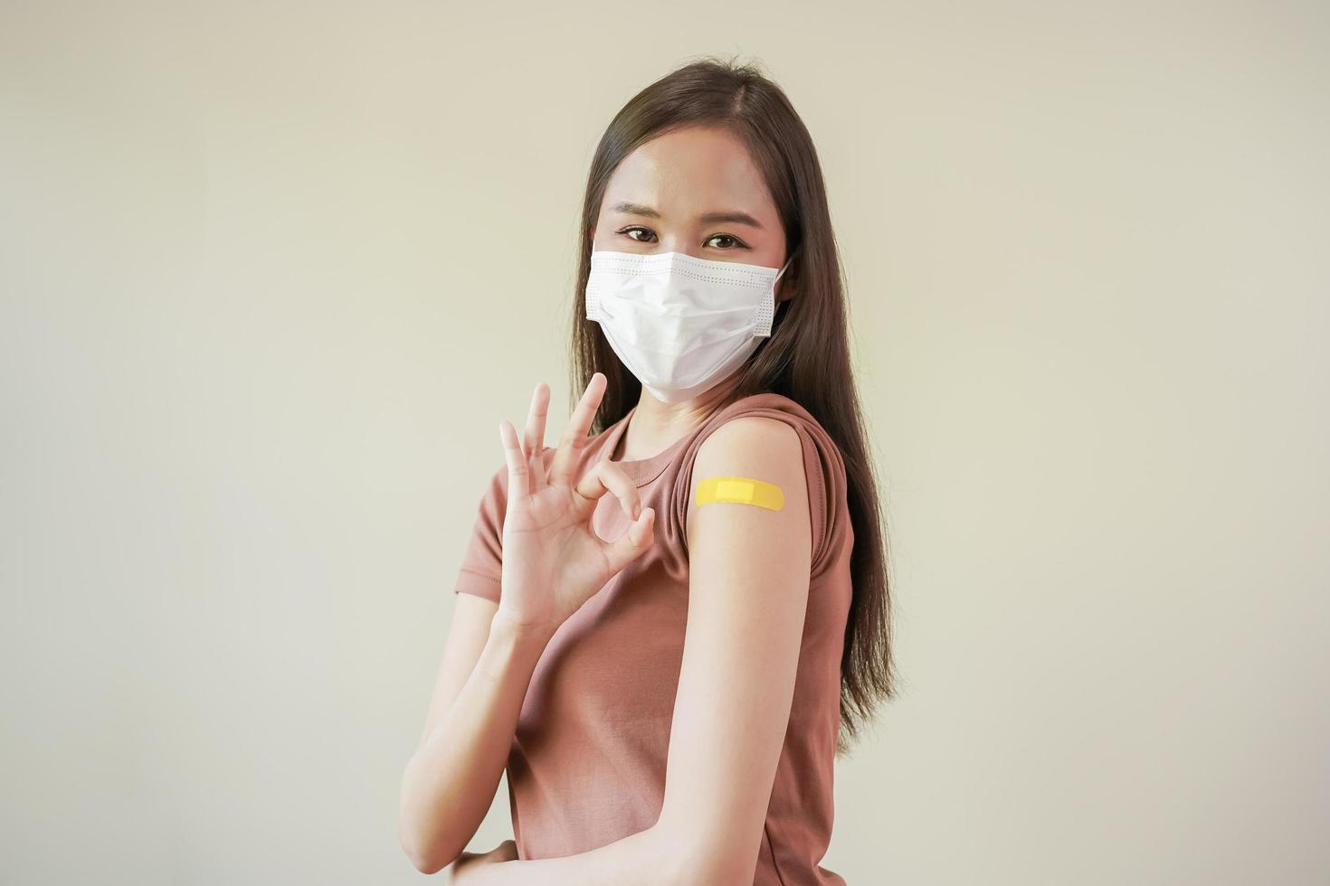 retrato de salud cuidado asiático joven mujer vistiendo cara máscara proteger, consiguiendo vacuna de COVID-19, influenza en casual, demostración brazo en amarillo vendaje, yeso, aislado en naturaleza fondo, Copiar espacio foto