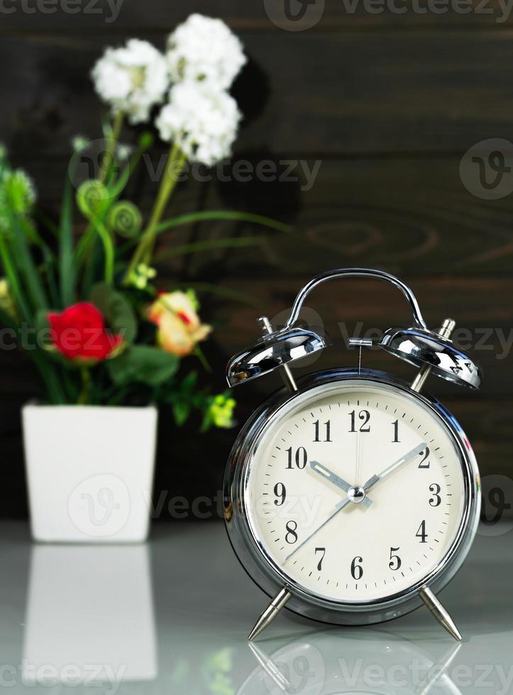 Alarm clock and flower vase on table photo