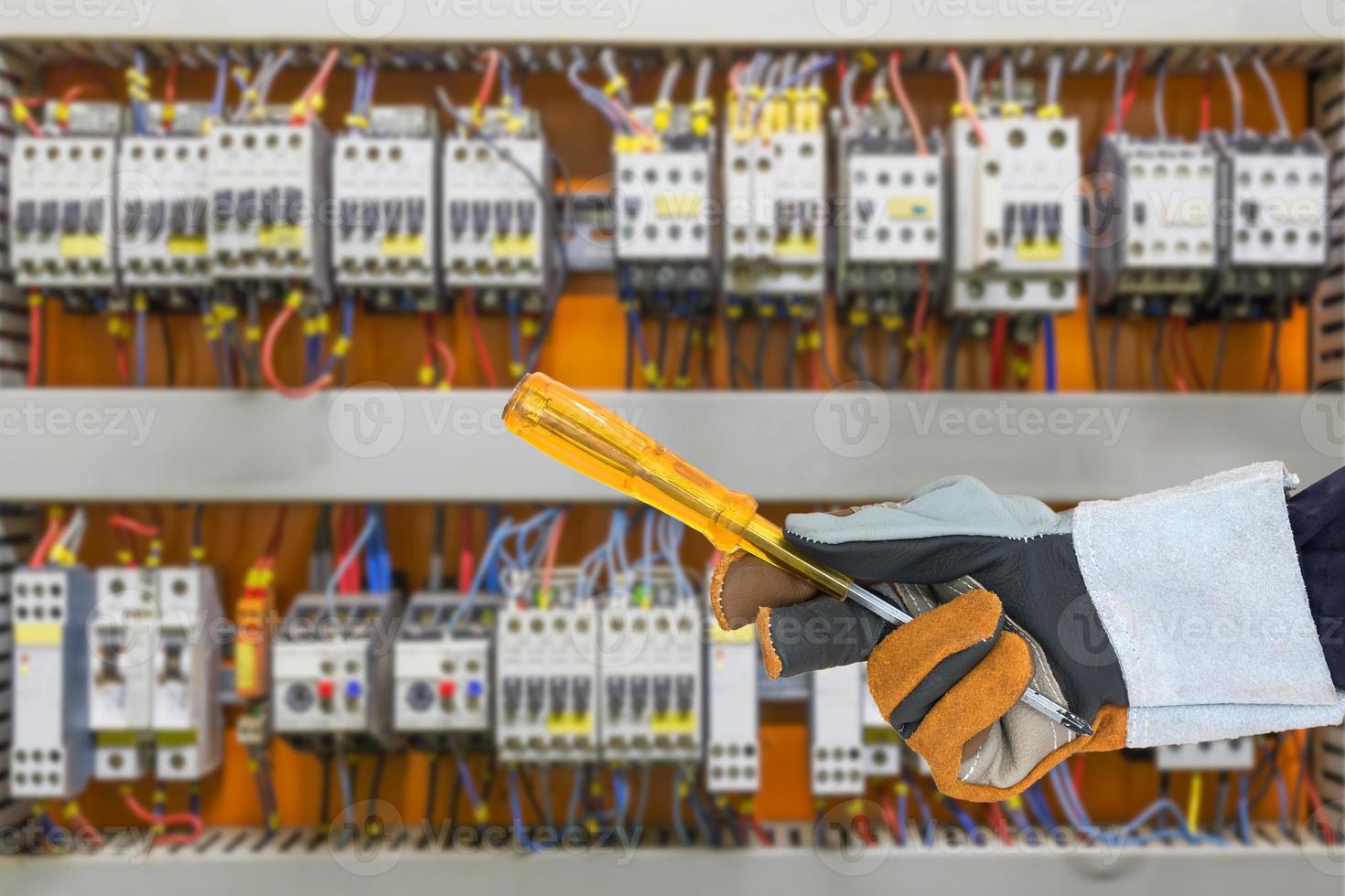 Hand in glove holding screwdriver with control panel cabinet photo