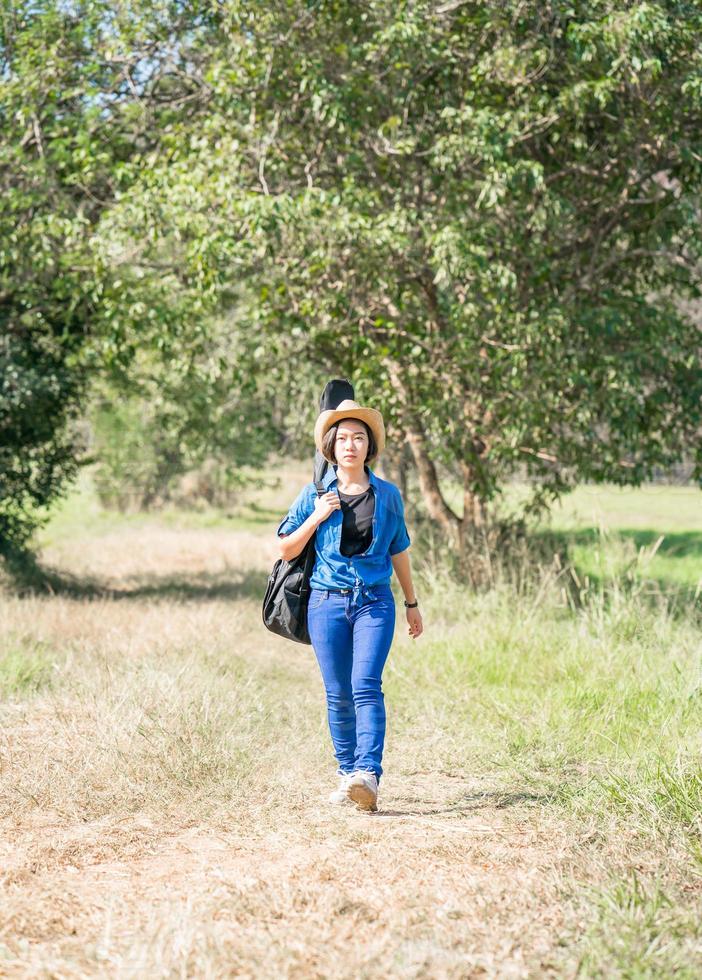 woman wear hat walking and carry her guitar bag photo