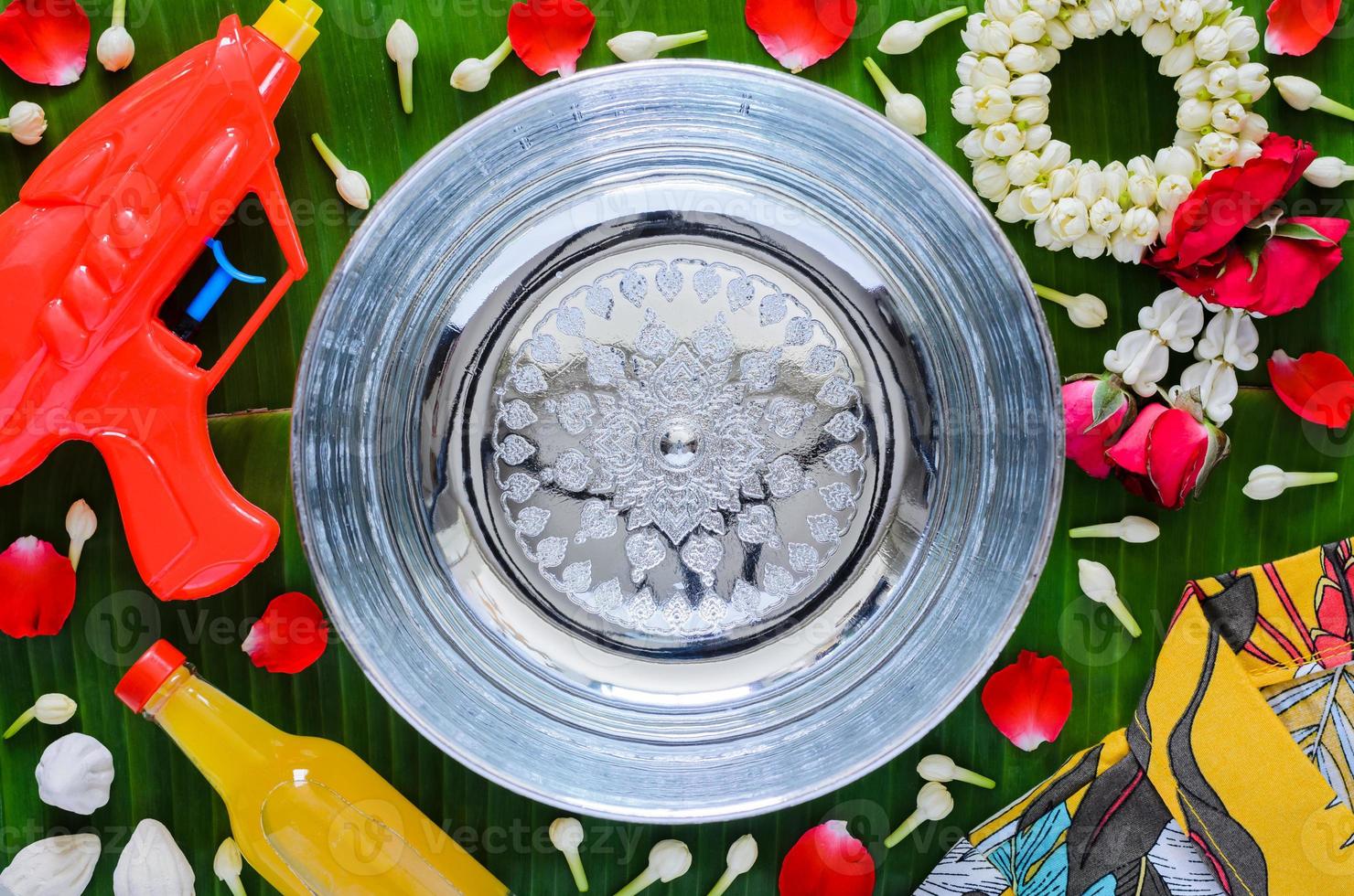 Thailand songkran festival background with water gun, garland, shirt, scented water that have space for text in water of blurred silver bowl put on banana leaf. photo