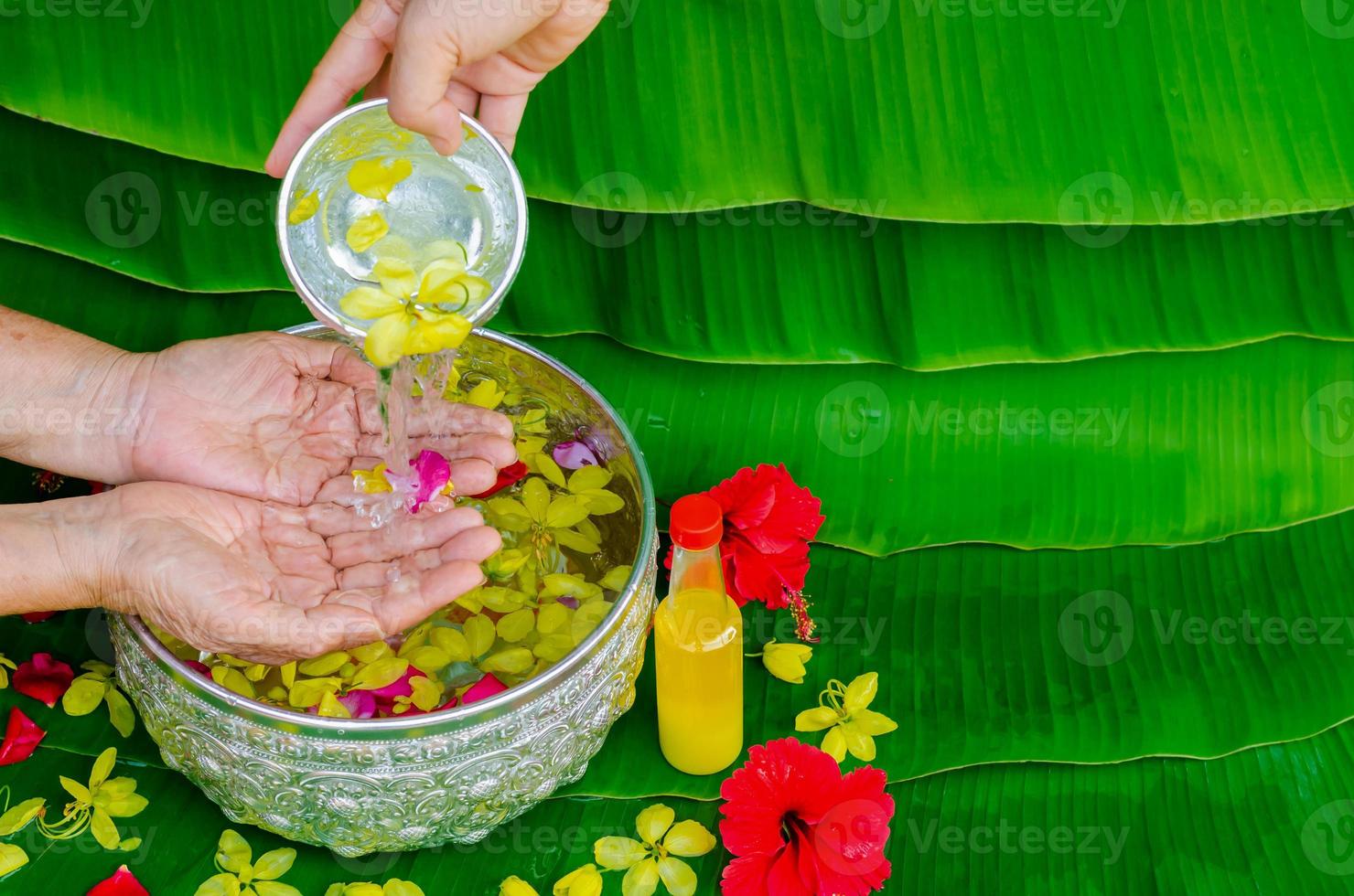 Songkran festival background with hand pouring water and flowers to elder people for blessing with scented water on wet banana leaf background. photo