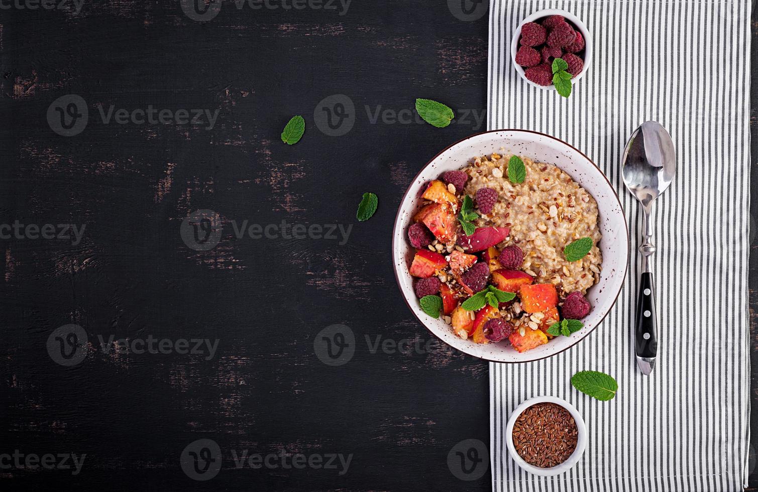 Oatmeal porridge with raspberry and peach on dark background. Healthy breakfast. Vegetarian food. Top view photo