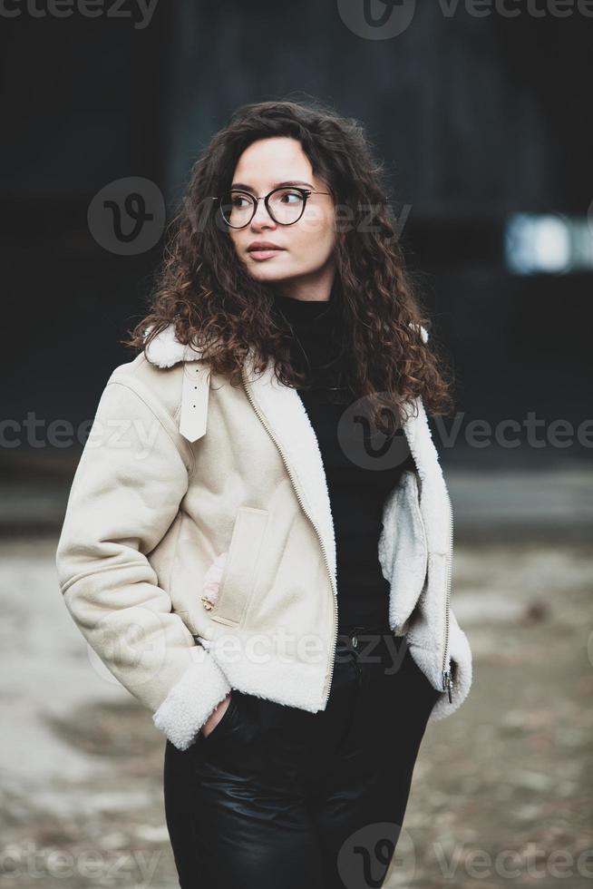 Beautiful young woman with brunette curly hair, portrait in eye glasses enjoying the sun in the city. photo