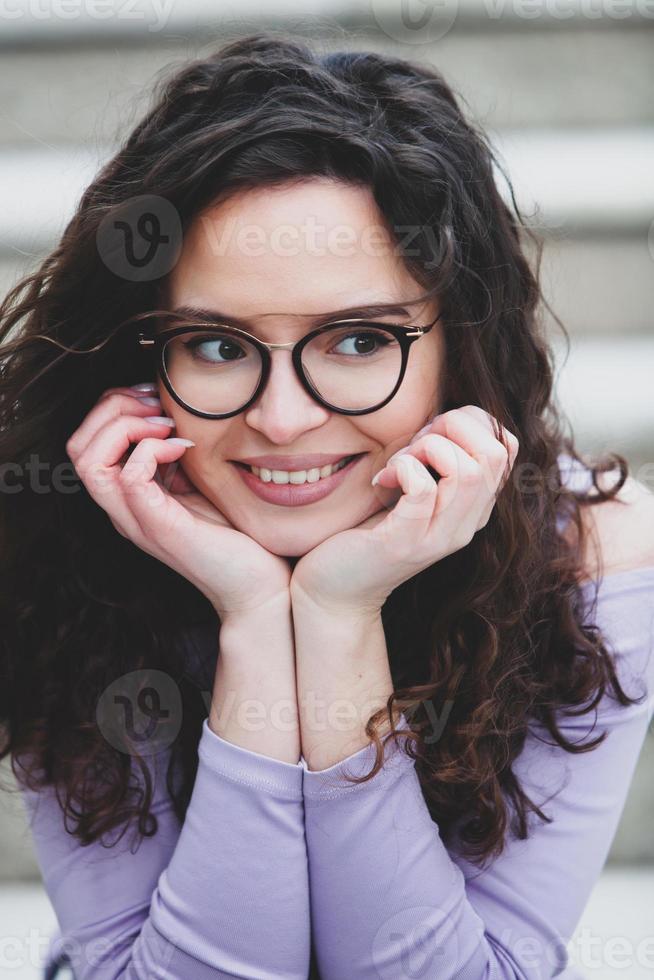 Beautiful young woman with brunette curly hair, portrait in eye glasses enjoying the sun in the city. photo