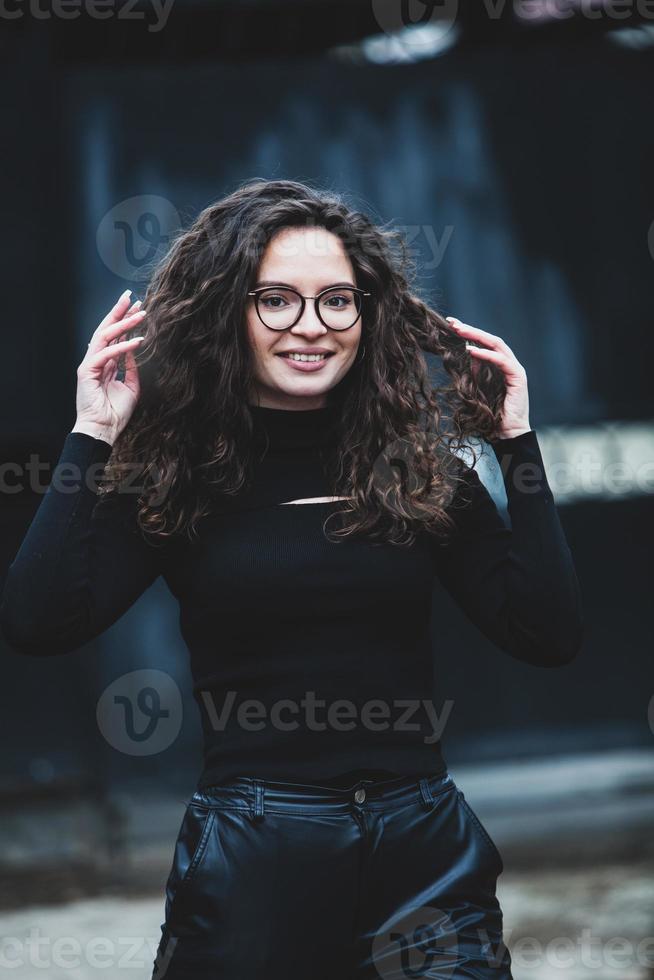 hermosa joven mujer con morena Rizado cabello, retrato en ojo lentes disfrutando el Dom en el ciudad. foto