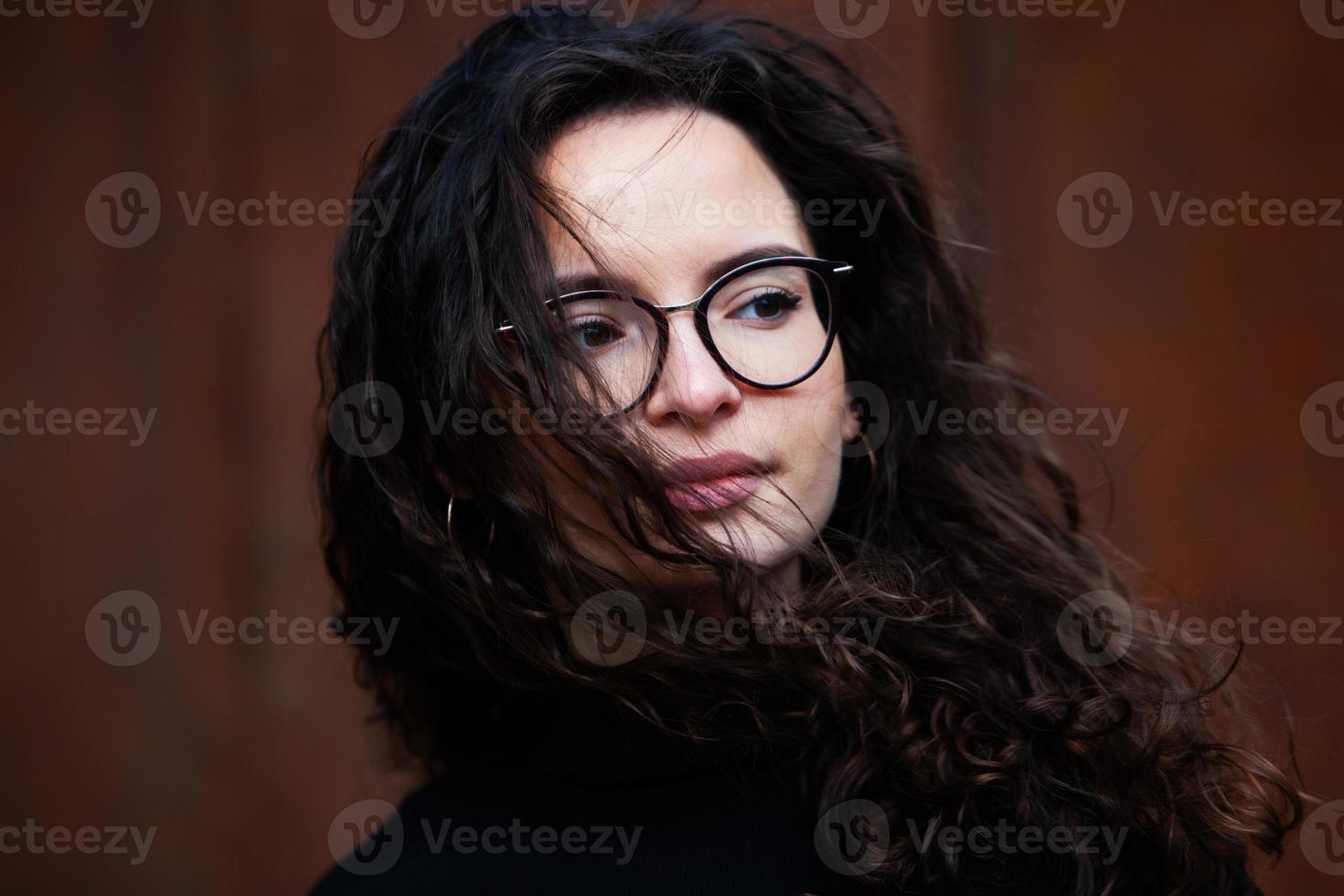 hermosa joven mujer con morena Rizado cabello, retrato en ojo lentes disfrutando el Dom en el ciudad. foto