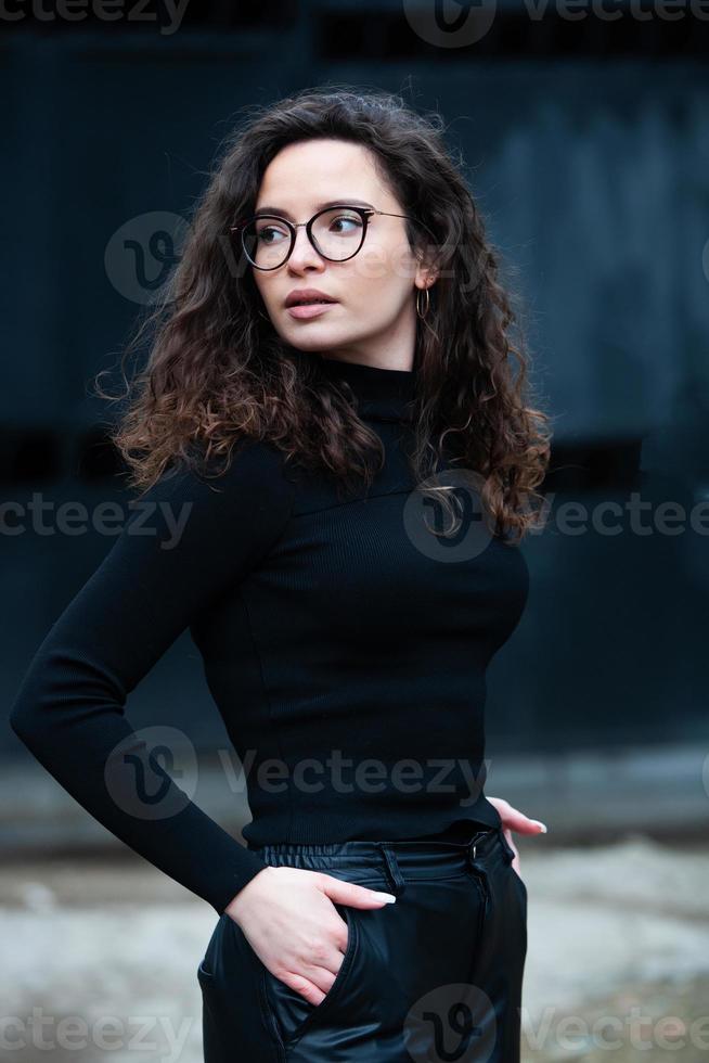 Beautiful young woman with brunette curly hair, portrait in eye glasses enjoying the sun in the city. photo