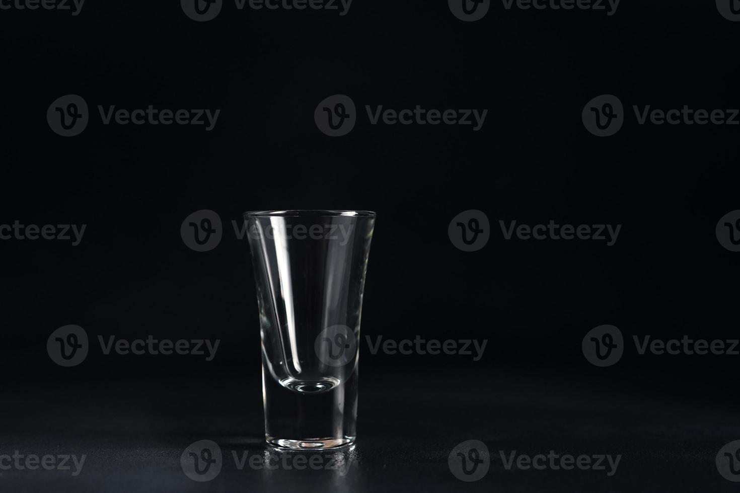 vacío vaso de vodka en negro antecedentes. un vacío bebida transparente vaso en un negro antecedentes. aislar. Copiar espacio foto