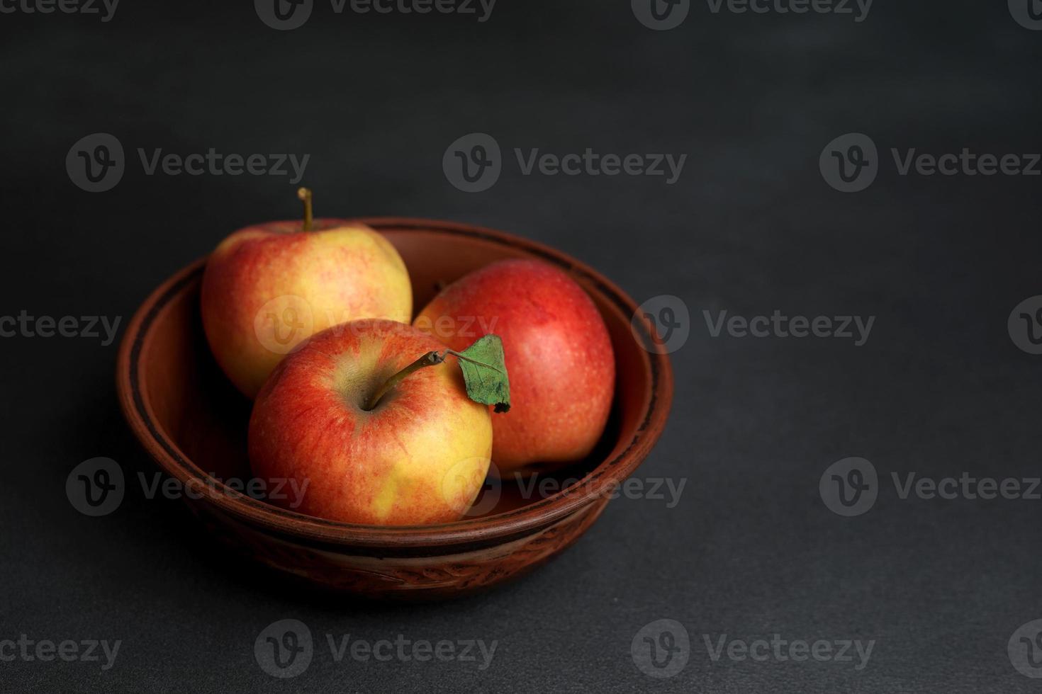 Tres rojo jugoso manzanas mentira en un arcilla plato en contra un negro antecedentes. Copiar espacio foto