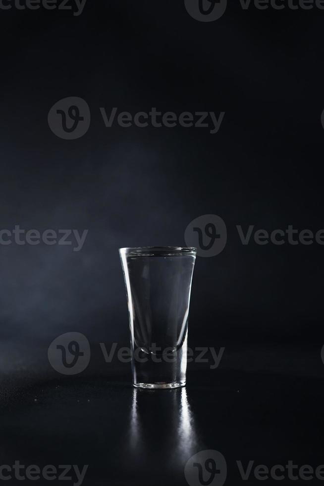 cerca arriba de vaso de vodka en un negro antecedentes. bebida transparente vaso en un negro antecedentes. aislar. Copiar espacio foto