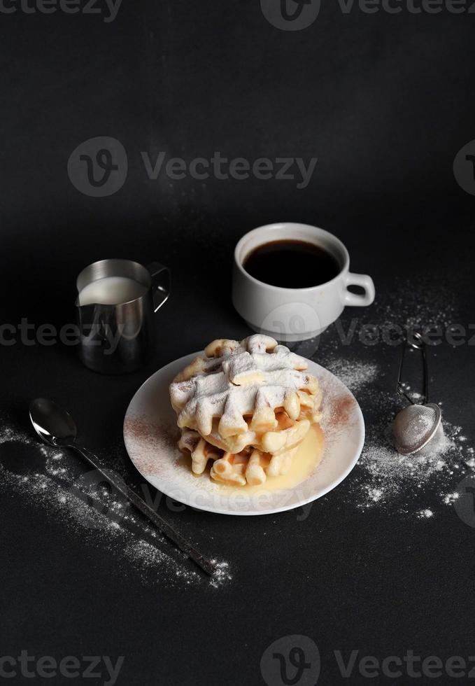 plato con hecho en casa gofres cubierto con en polvo azúcar, caramelo salsa, taza de café, Leche en un gris antecedentes foto