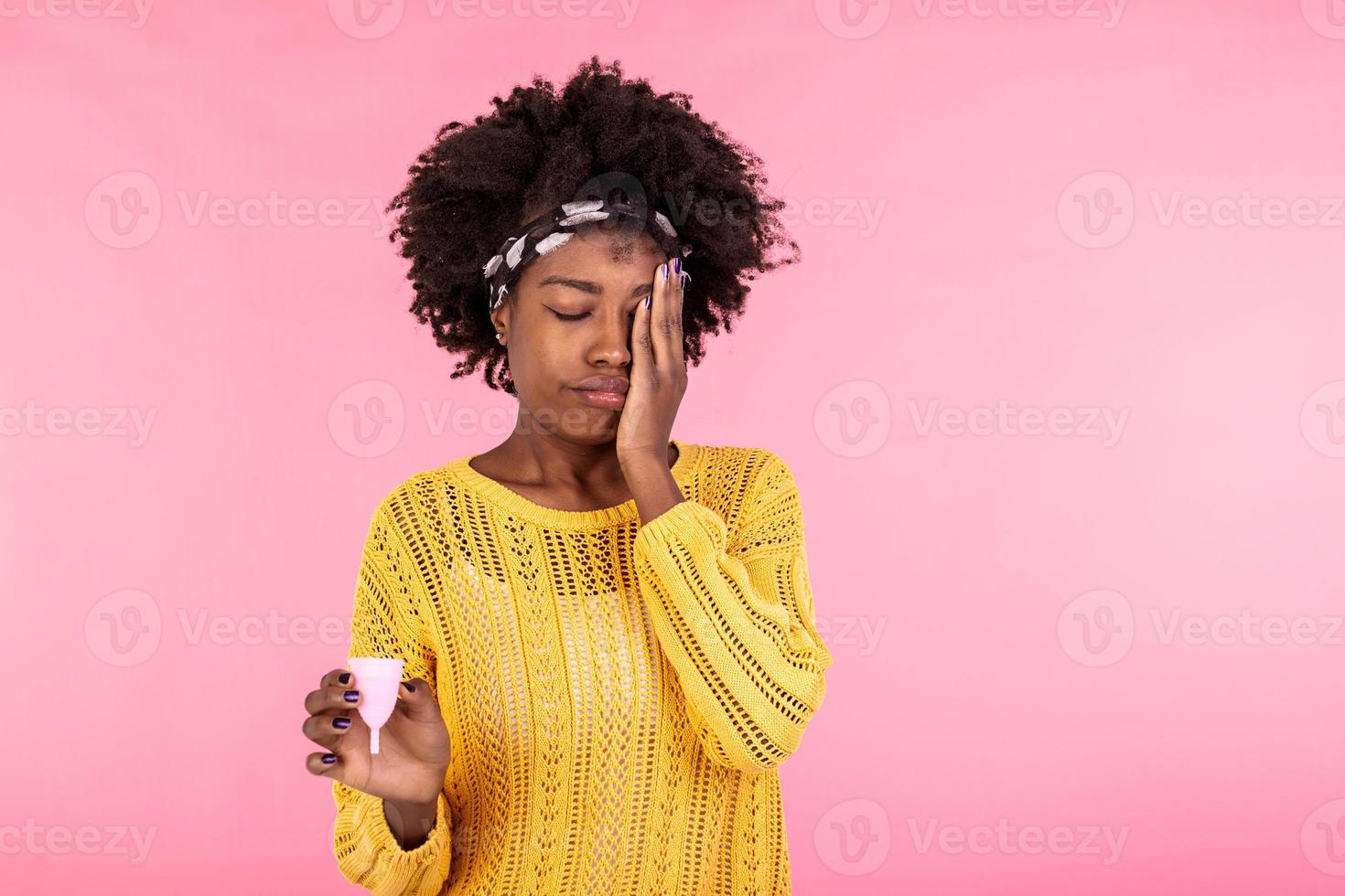 Pensive African American woman holds effective safe affordable menstrual product, good protection from leakage, chooses reusable menstrual cup, thinks how to use it, blank empty space on pink wall photo
