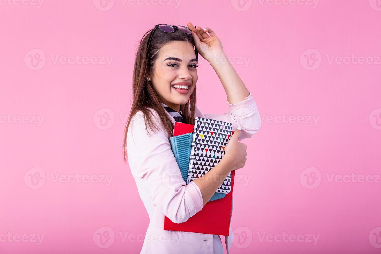 Young female student in glasses holding books in hand isolated on pink background portrait, casual daily lifestyle student holding notebooks smiling photo