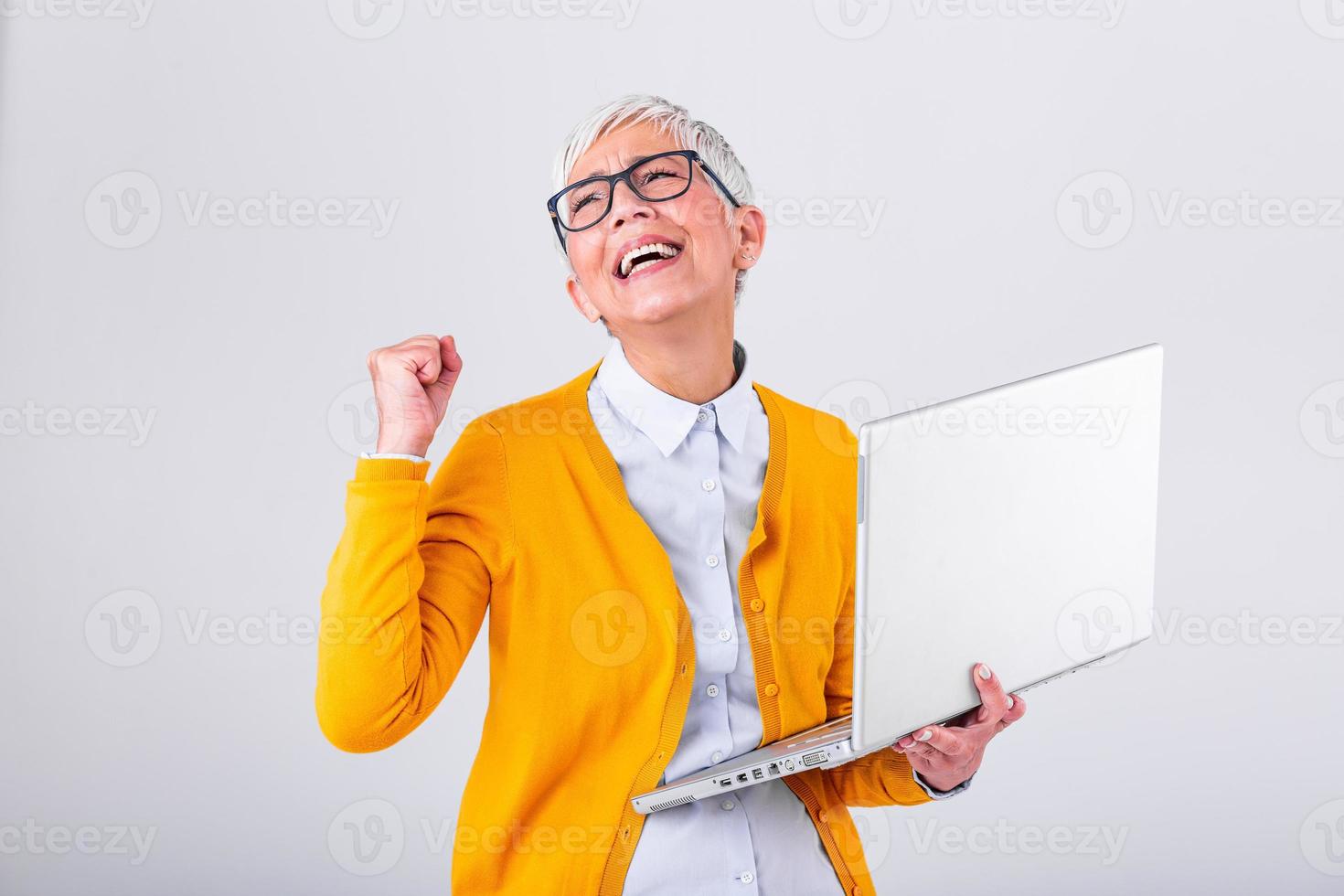 woman with a laptop computer and celebrating success isolated over gray background. Photo of senior cheerful business woman standing over grey wall with laptop computer.