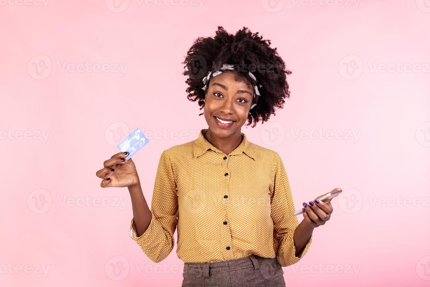 retrato de un africano americano mujer en pie en un rosado antecedentes participación teléfono inteligente y dinero, devolución de dinero. mujer participación dinero y pago en línea en su móvil teléfono foto