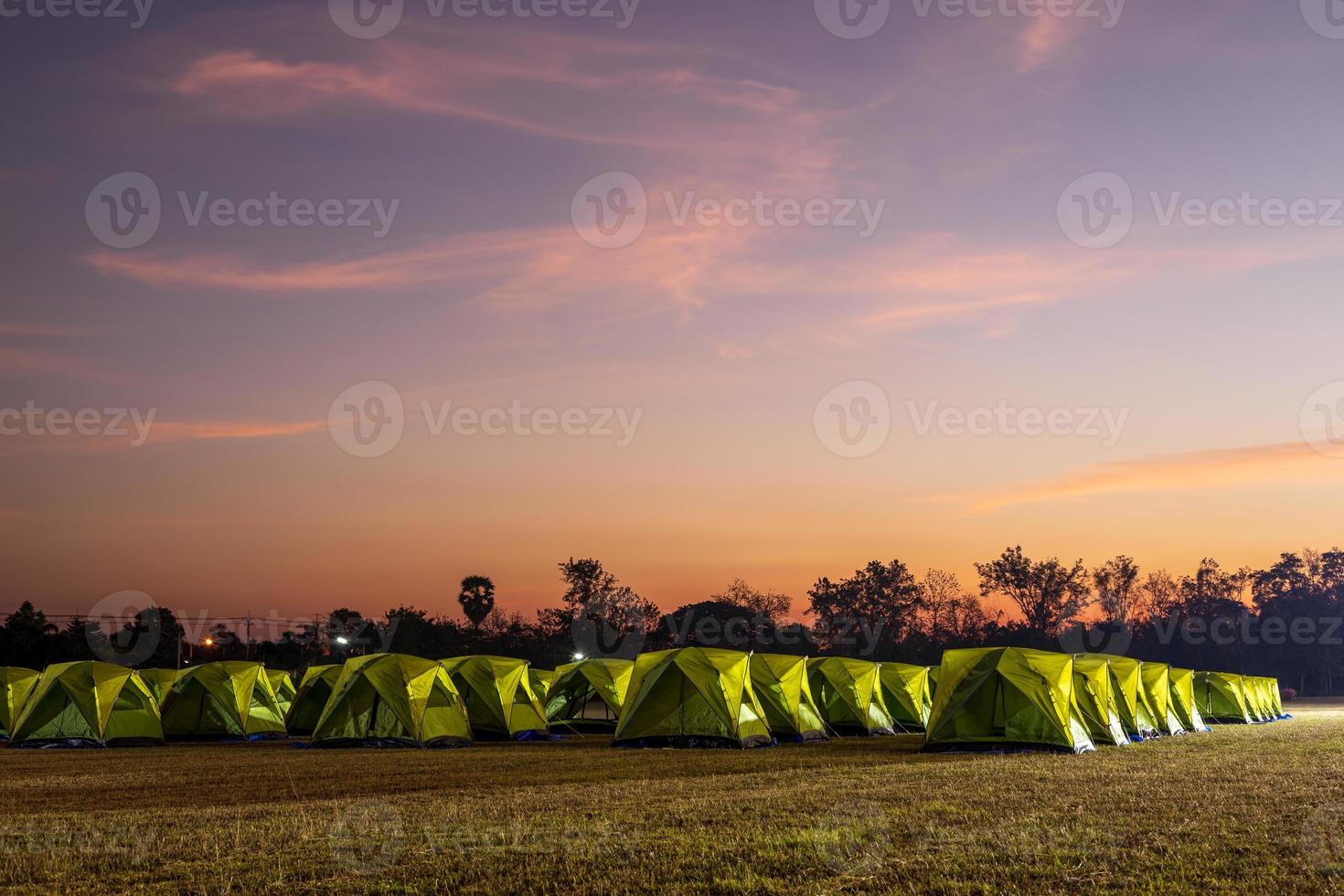 Scenery of rows of green canvas camping tents with floodlights installed on the lawn. photo