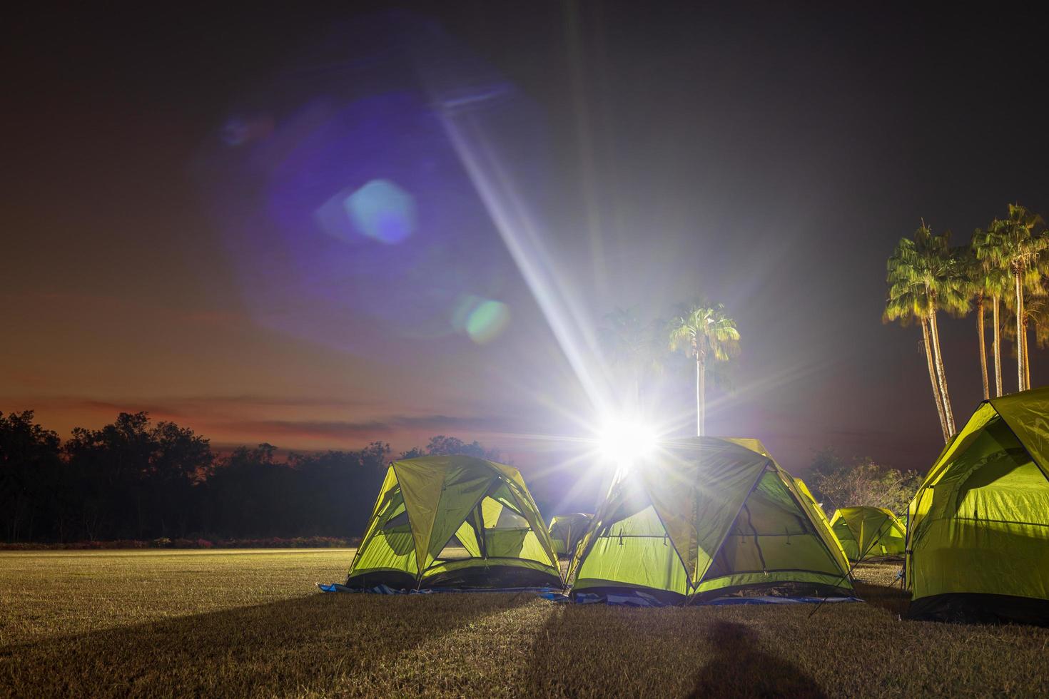 A view of a green canvas camping tent illuminated by floodlights set up on the lawn. photo