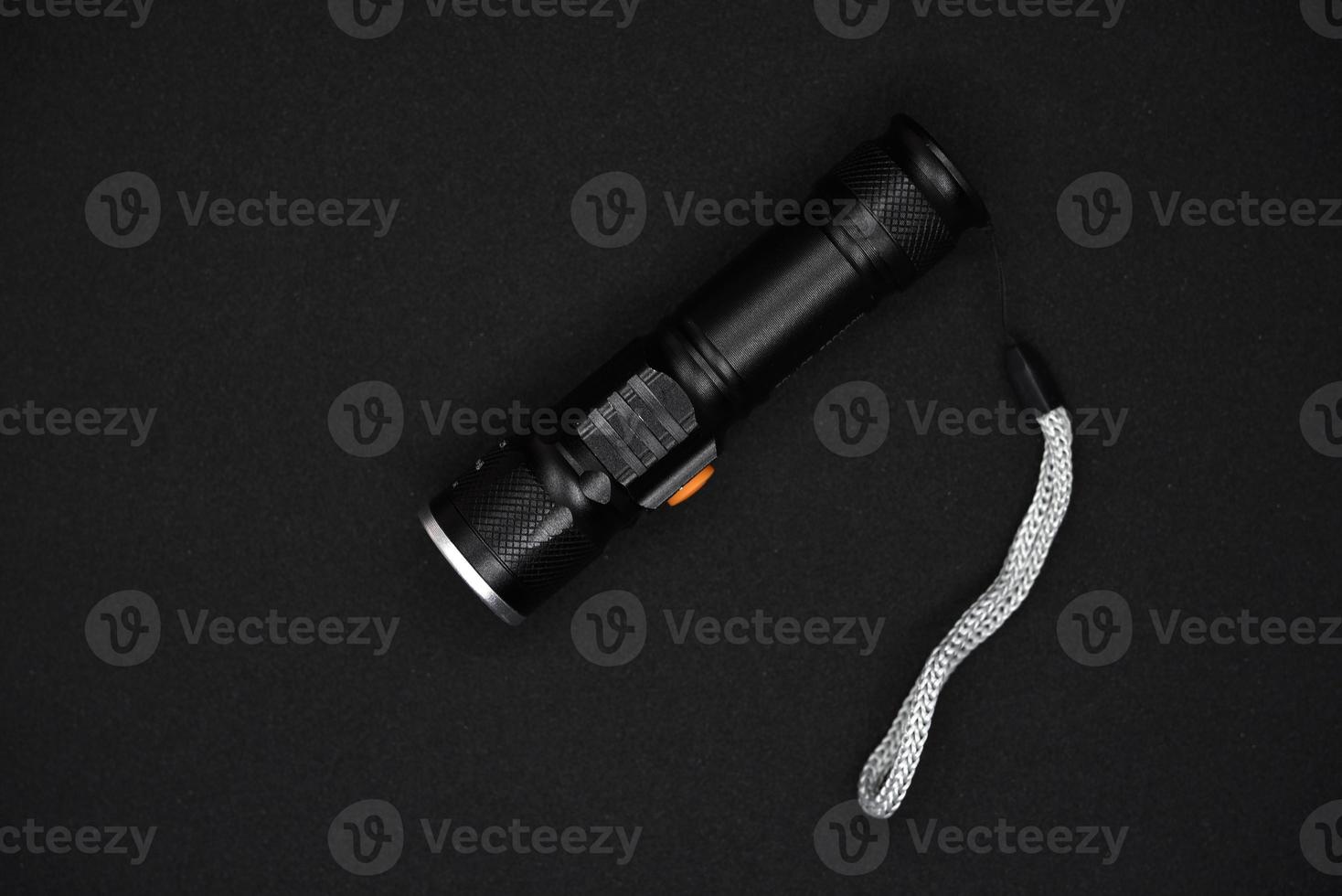 Metal black flashlight on a black background. Pocket flashlight