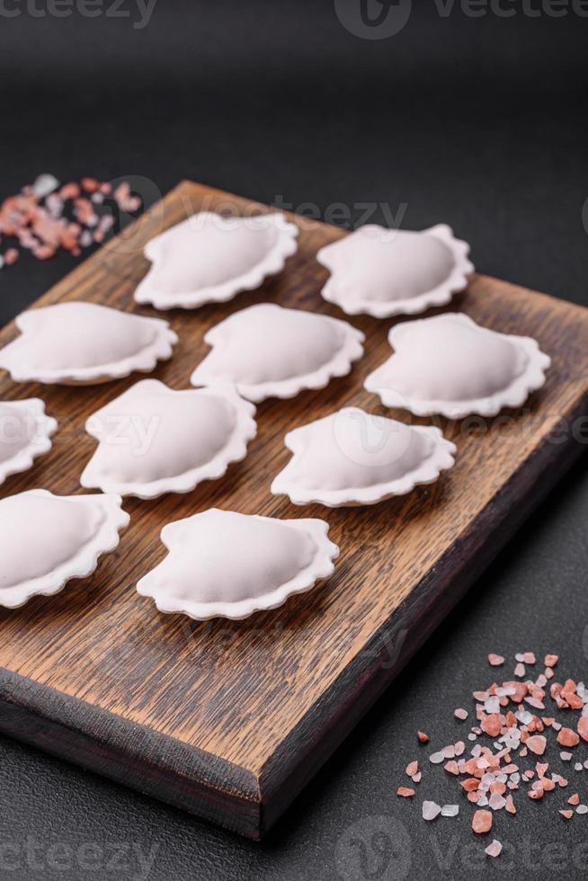 Raw frozen stuffed dumplings on a wooden cutting board photo