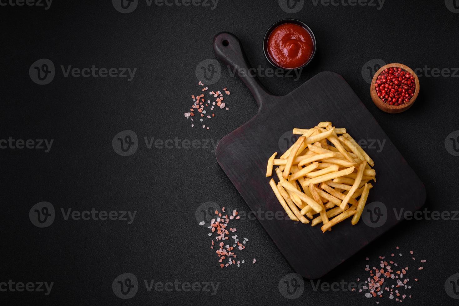 Delicious crispy french fries with salt and spices on a dark concrete background photo