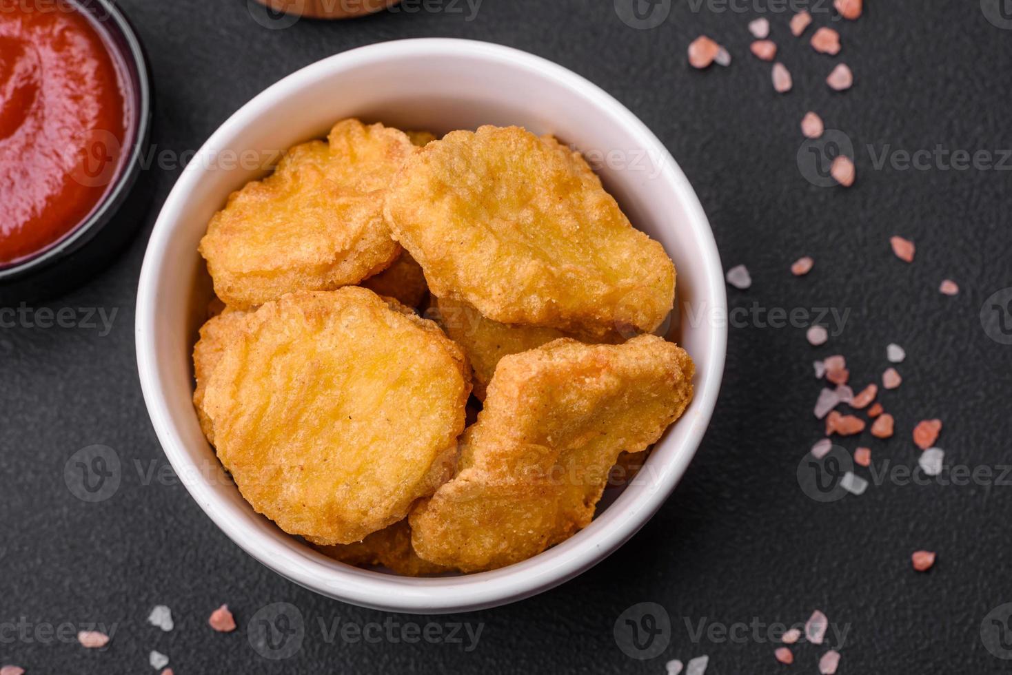Delicious crispy chicken nuggets with salt and spices on a dark concrete background photo