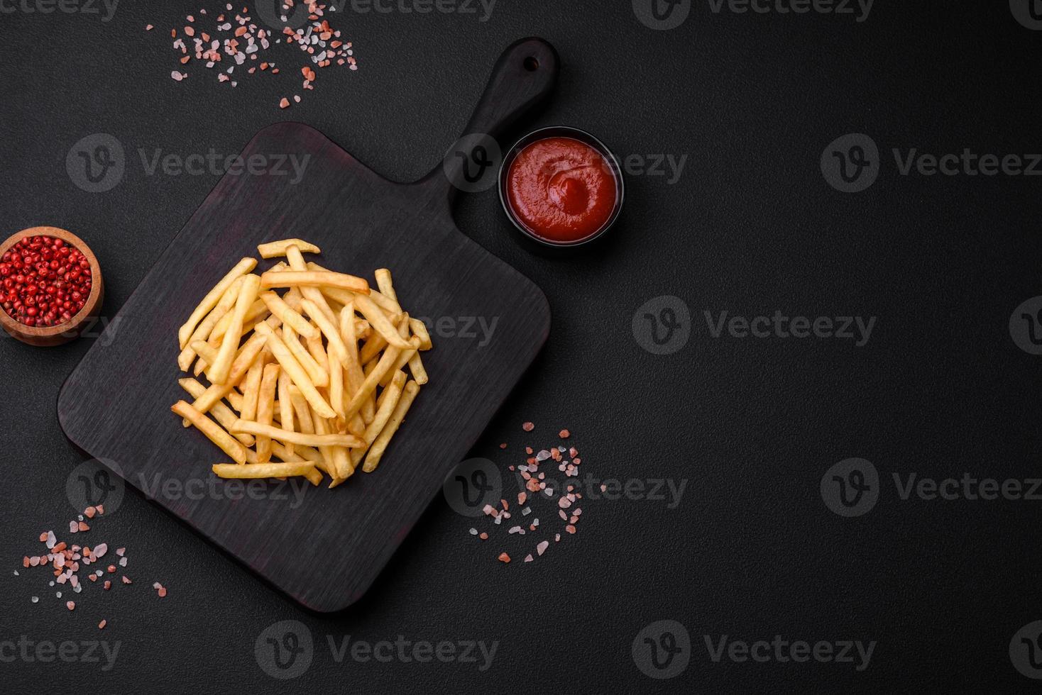 Delicious crispy french fries with salt and spices on a dark concrete background photo