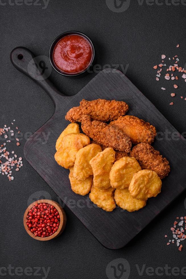 Delicious crispy chicken nuggets with salt and spices on a dark concrete background photo