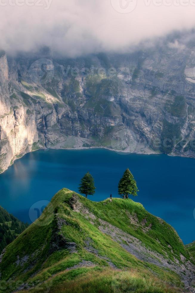 A blue mountain lake surrounded by mountains, a person stand in the distance photo