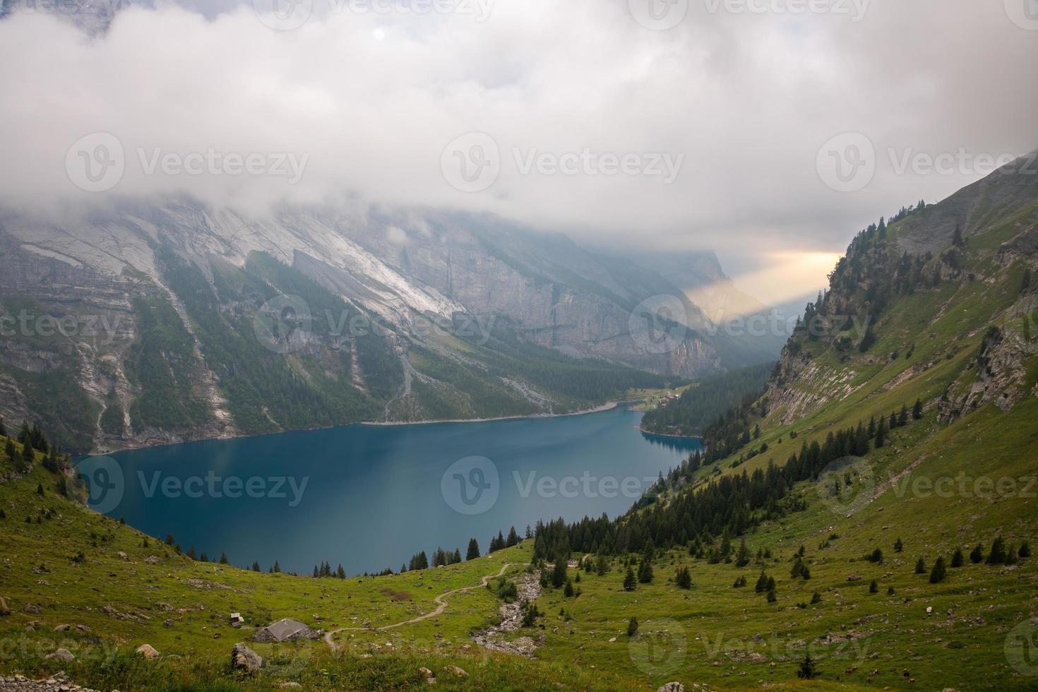 un montaña lago oeschinensee debajo un nublado cielo, un grande rayo de sol rompe mediante el nubes foto