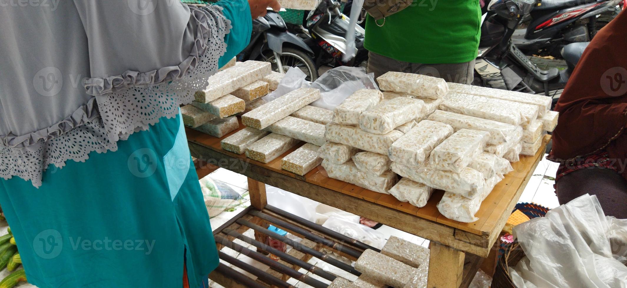 tempe mentah. raw tempeh, uncooked soybean cake from indonesia in a plastic on the table. transaction in traditional market. photo