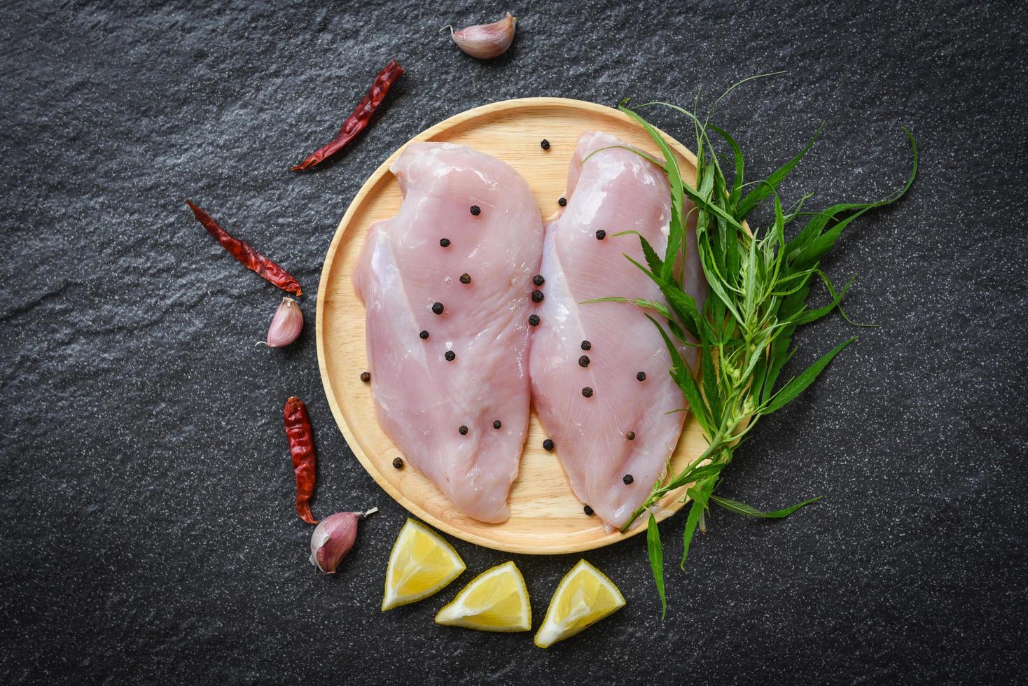 raw chicken breast with marijuana leaf cannabis herbs and spices on wooden plate - fresh uncooked chicken meat marinated with ingredients for cooking photo