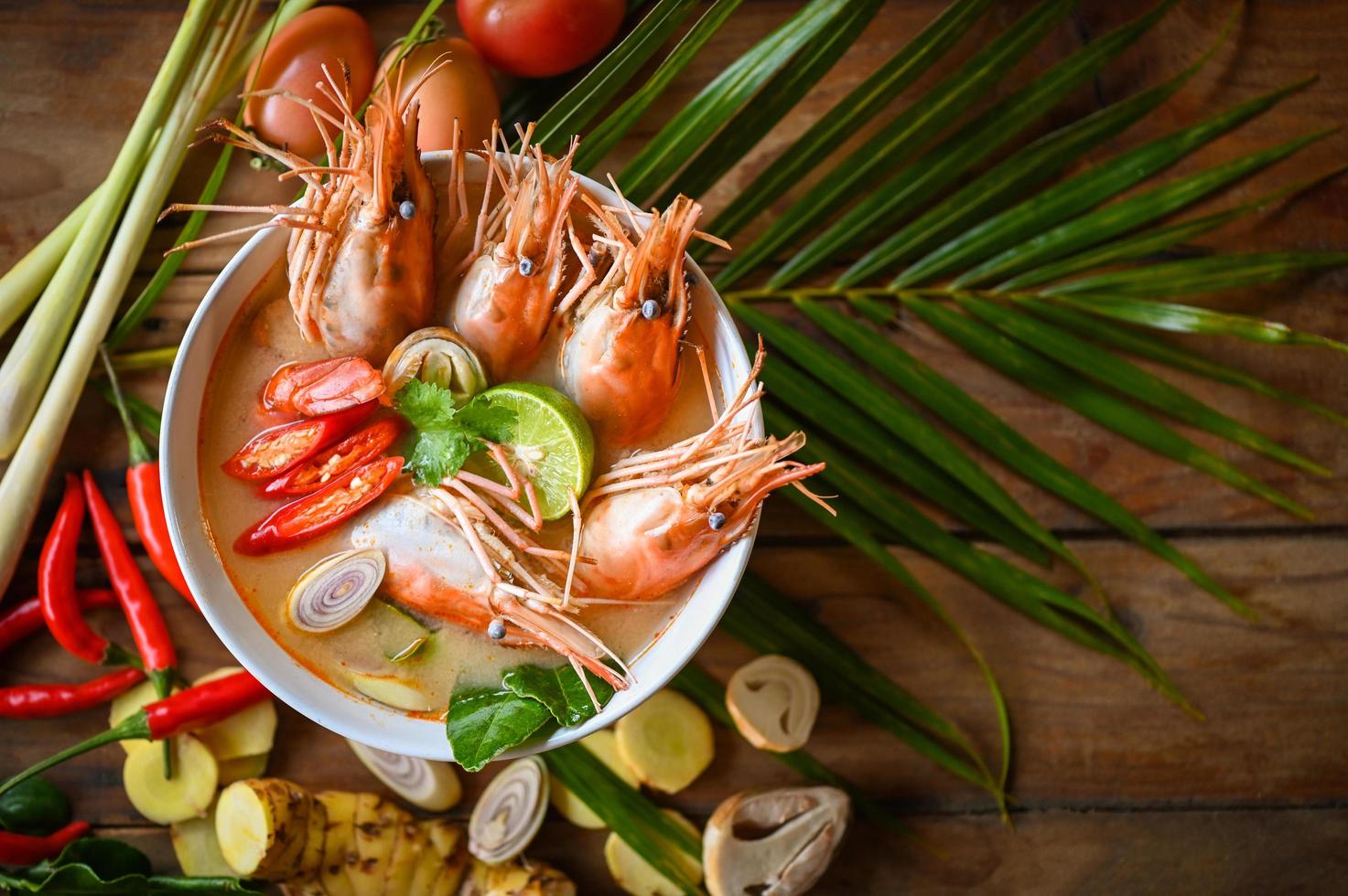 Shrimp soup on seafood soup bowl with thai herb and spices, Hot and sour spicy shrimps prawns soup  curry lemon lime galangal red chili straw mushroom on table food, Thai Food Tom Yum Kung photo