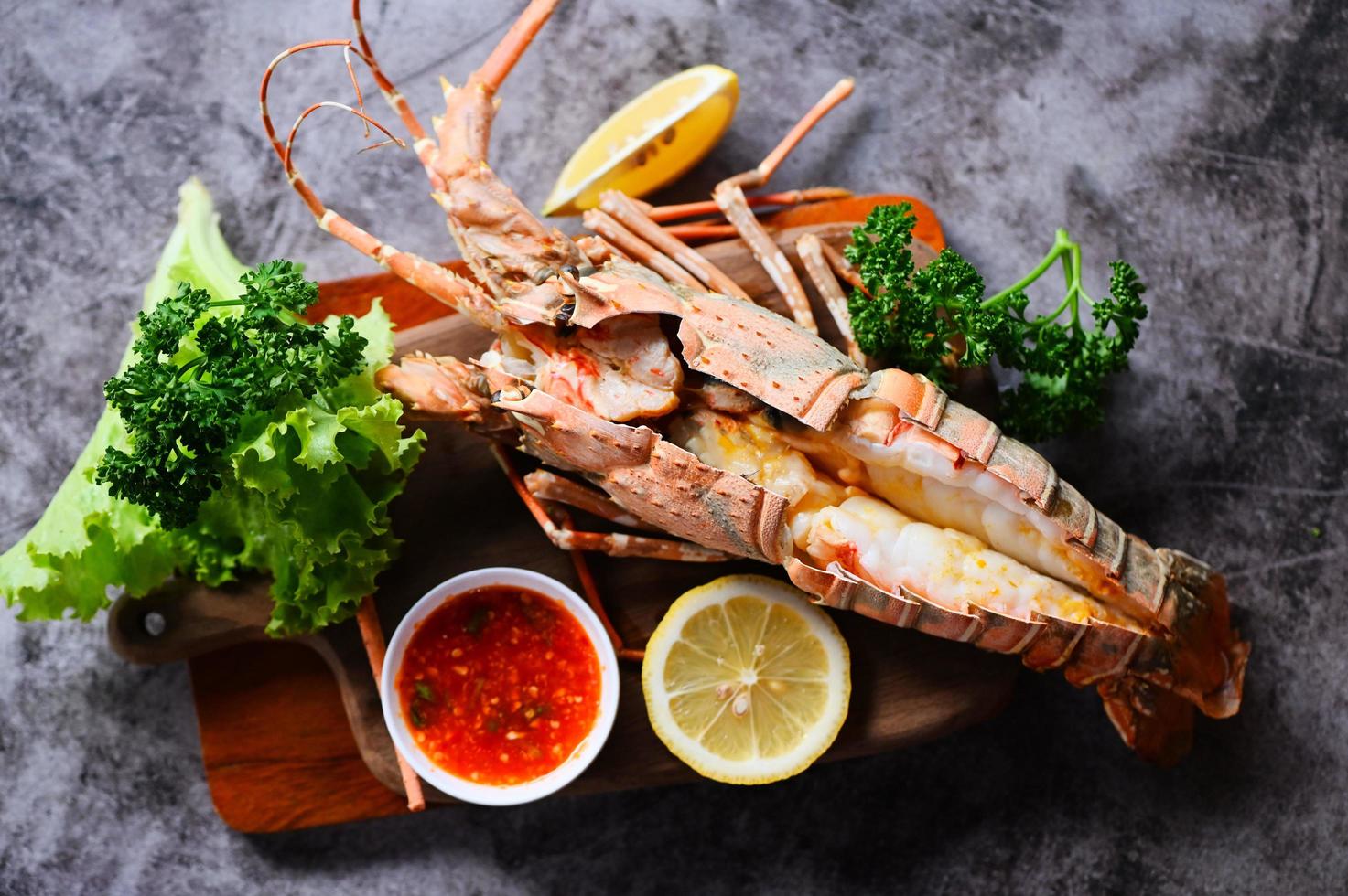 spiny lobster food on wooden cutting board, fresh lobster or rock lobster seafood with herb and spices lemon coriander parsley on dark, lobster for cooking food and seafood sauce photo