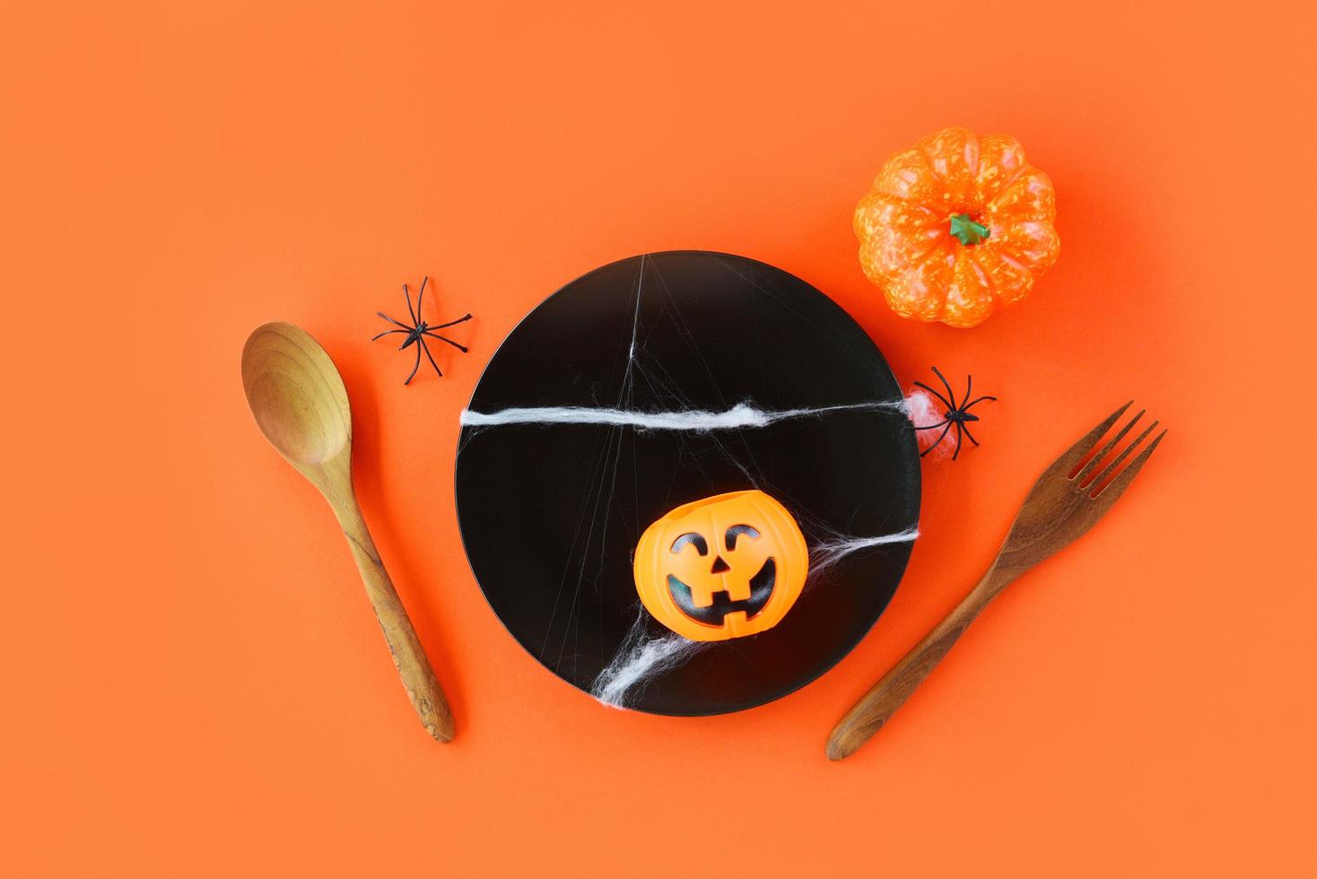 Halloween table setting decoration accessories holiday with spider spoon fork and pumpkin jack o lantern in black plate on orange background halloween dinner top view photo