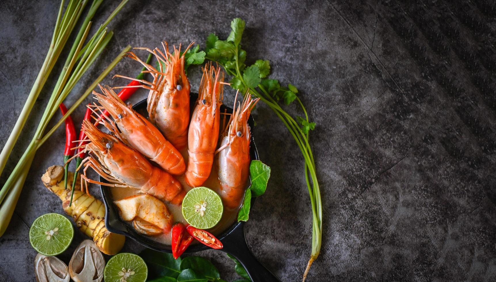 Shrimp soup on seafood soup bowl with thai herb and spices, Hot and sour spicy shrimps prawns soup  curry lemon lime galangal red chili straw mushroom on table food, Thai Food Tom Yum Kung photo