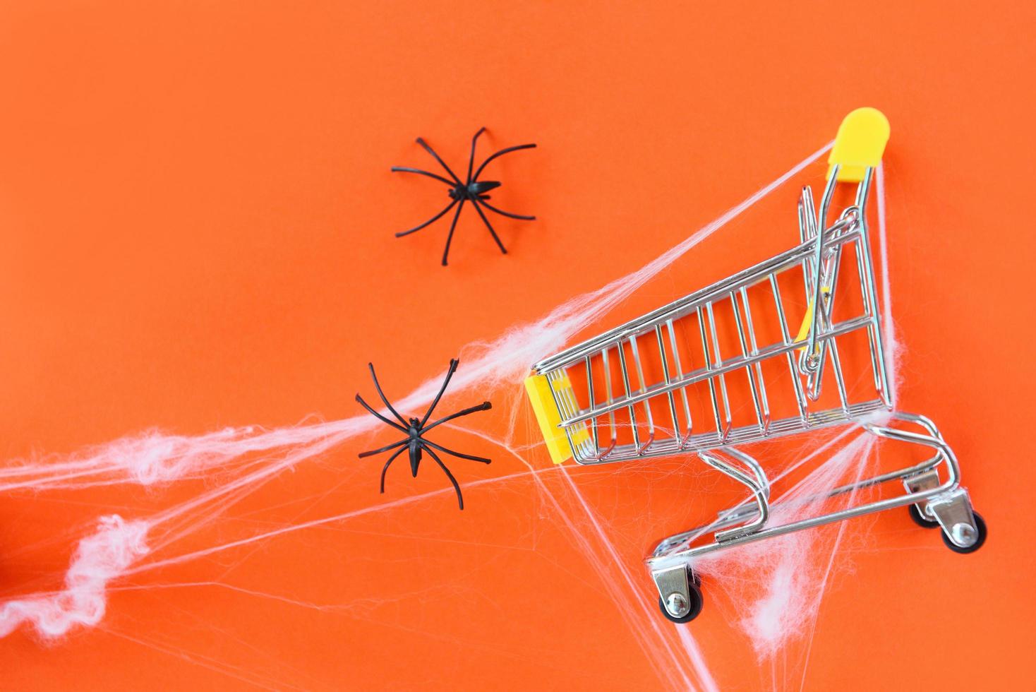 Halloween shopping holiday concept - accessories with black spider and spider web on shopping cart on orange background , top view aerial image flat lay photo