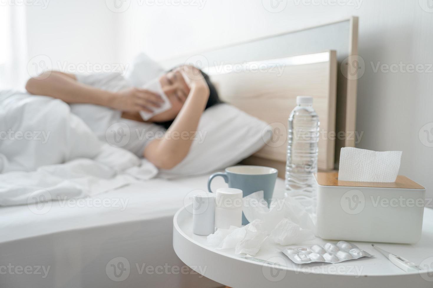 Asian woman feeling sick while lying in blanket on bed She coughed and sneezed with a tissue and touched her forehead. photo